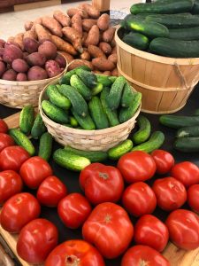 Colorful assortment of fresh vegetables including tomatoes, cucumbers, and sweet potatoes at a market.