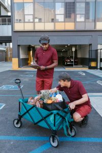 Two delivery workers in uniforms checking and organizing groceries in a cart outdoors.